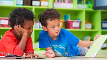 Two elementary boys looking at picture book together in front of classroom library
