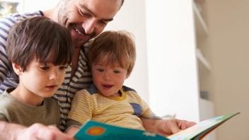 Dad reading picture book to kindergarten and preschool sons