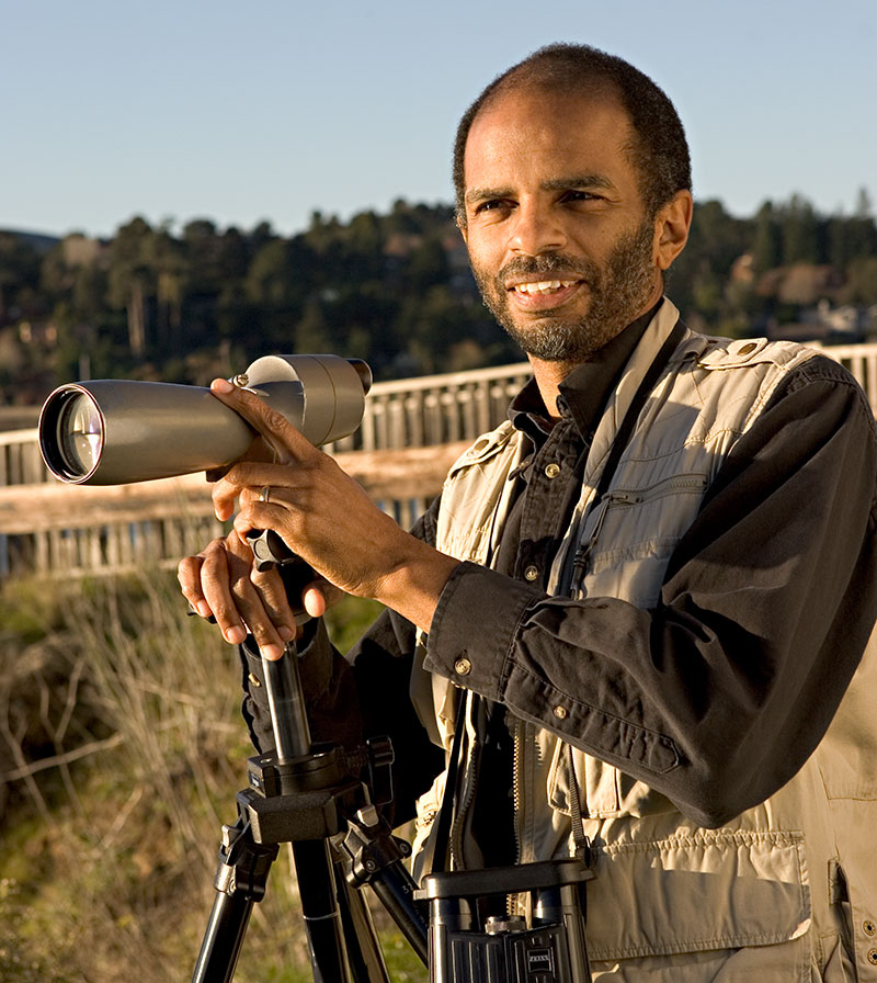 Ornithologist and wildlife biologist John C. Robinson outside wearing sport vest and with spotting scope and binoculars