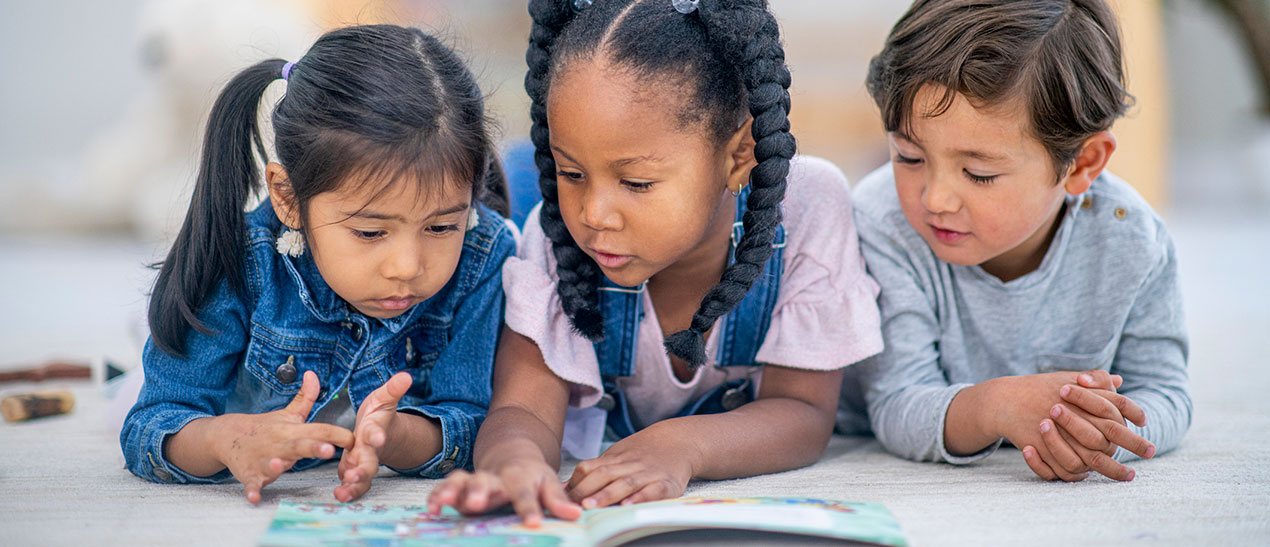 three young multicultural kids reading a picture book together