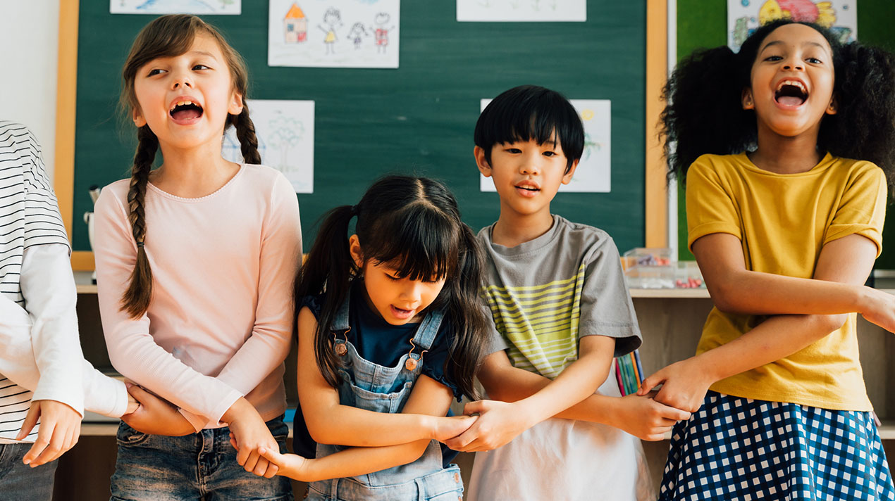 Multicultural elementary kids linking arms in classroom