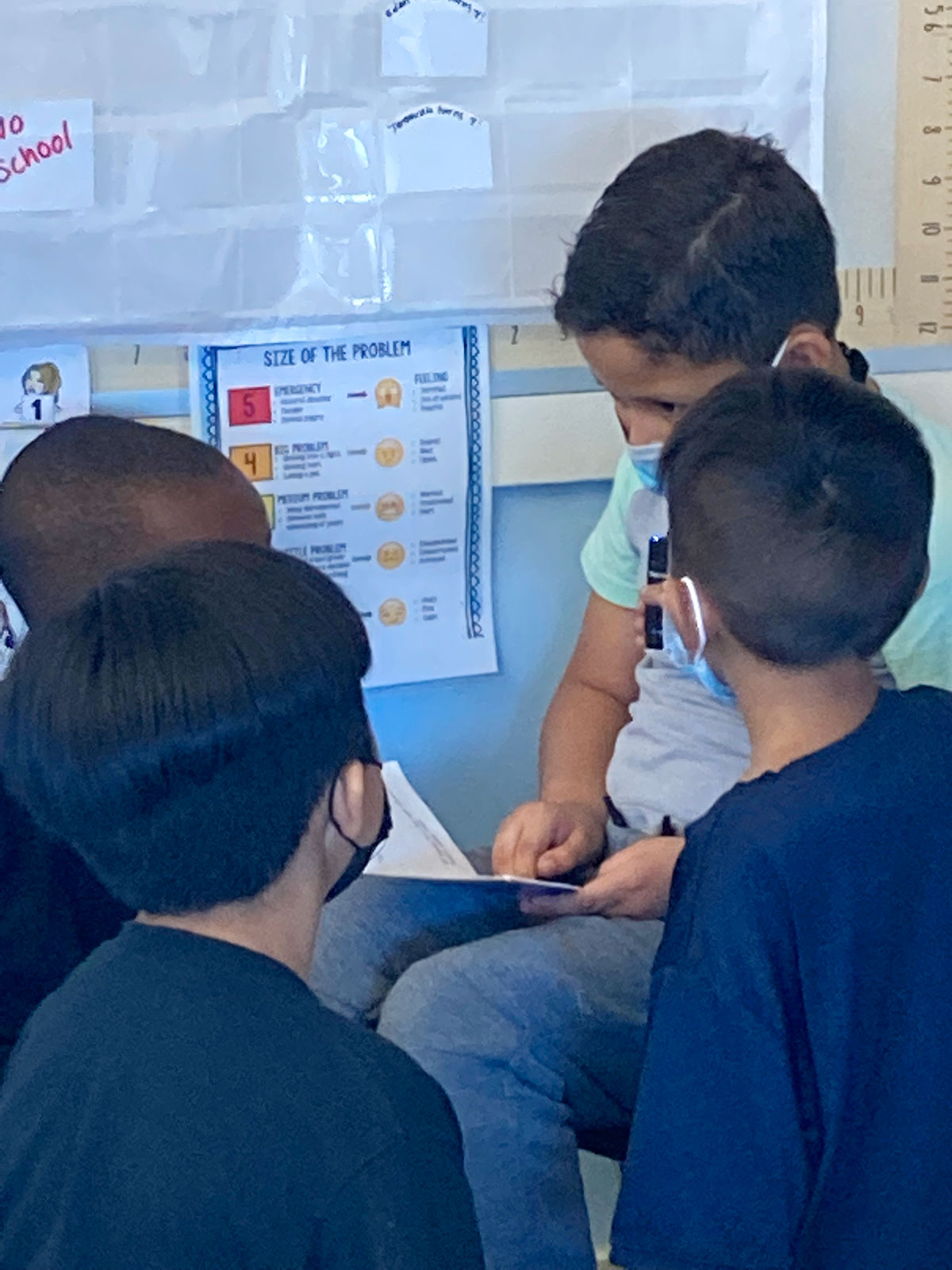 Small group of multicultural students listening to classmate read aloud