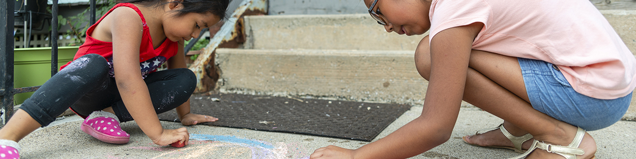 Two elementary-aged Latina children doing chalk drawings