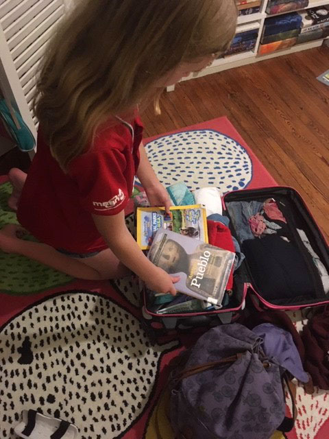 Young girl packing books for summer road trip to National Parks in Colorado
