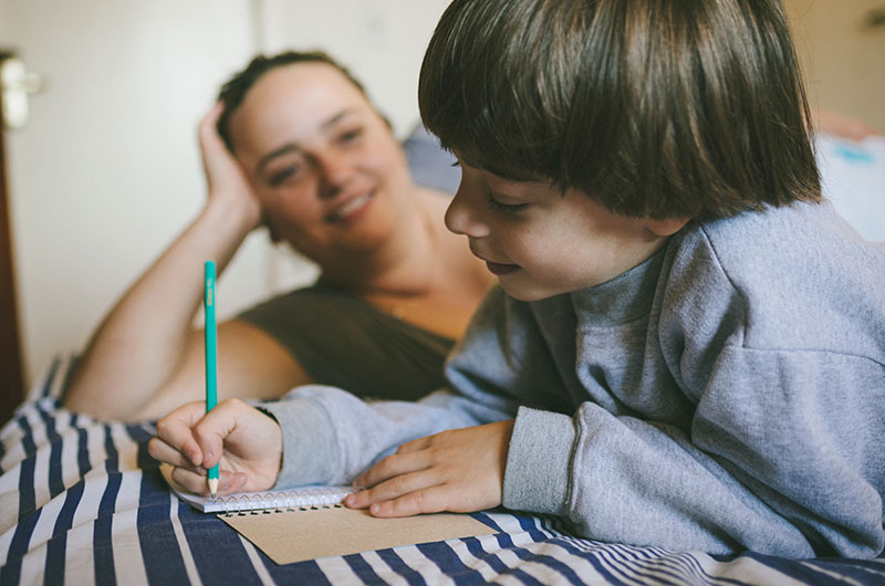 6 year old boy writing in a notebook with mother watching