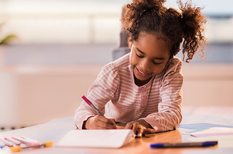 5 year old girl writing at her desk at home