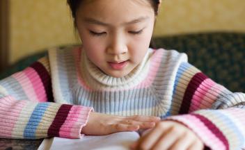 Elementary girl in colorful striped sweater reading a book