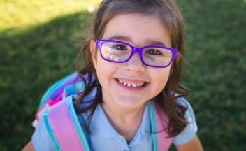 Young elementary girl wearing purple glasses and a backpack