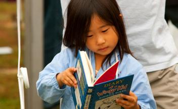 Young Asian girl reading The Wimpy Kid book