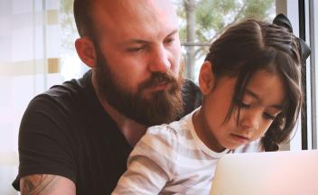 Elementary aged girl looking at laptop with her father