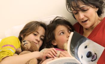 mother reading book about polar bears to her two young children in bed