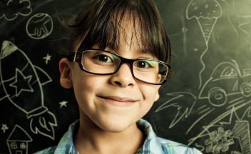Young girl looking at camera with blackboard full of science chalk drawings behind her