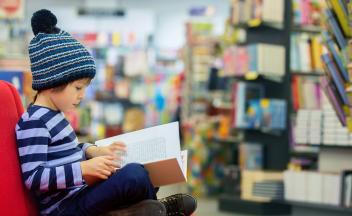 child with striped shirt and knit cap reading books at the library