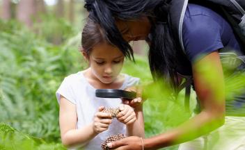 Mother and daughter looking at pine cones with magnifying glass outside