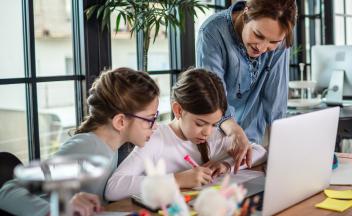 Mother helping two daughters with homework and writing at home