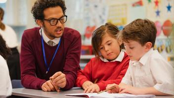 Male elementary teacher working with two students on a lesson
