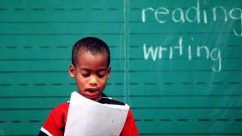 Young African American student reading aloud in front of a chalkboard