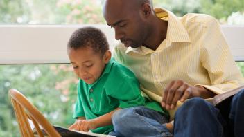 Black father reading picture book with young son
