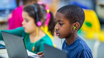 Elementary students using computers with headphones in classroom