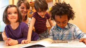 Teacher with diverse group of 3 students reading a picture book