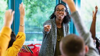 elementary teacher in lively conversation with students who have hands raised