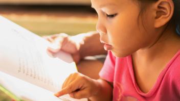Young girl pointing at text as she reads aloud