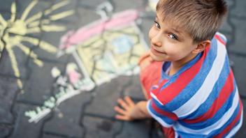 Young boy looking at camera with his chalk drawing in the background
