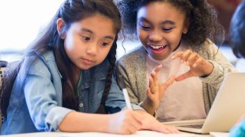 two elementary girls talking and writing in class