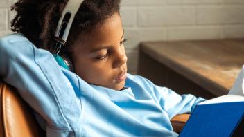 Young child wearing headphones will reading printed book