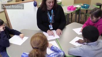 elementary teacher reading a text along with students around a table