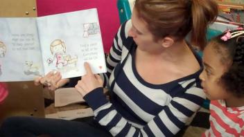 kindergarten teacher pointing at word in picture book during read aloud