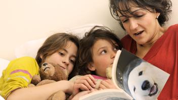 mother reading book about polar bears to her two young children in bed