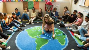 diverse group of elementary students learning about geography with world map on the floor