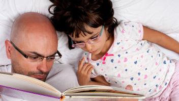Bird's eye view of father reading picture book to daughter