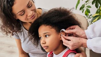 young girl being fitted for hearing aids with her mother