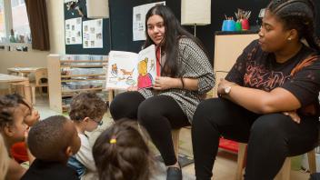 two preschool teachers doing a read aloud for a group of young kids