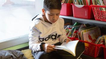 Elementary school aged boy reading a book beside classroom library bins