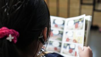 Young girl with hearing aid reading a graphic novel