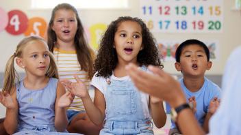 diverse group of kindergarten children clapping with teacher