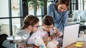 Mother helping two daughters with homework and writing at home