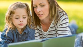 Mom reading picture book outside with elementary-aged daughter