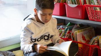 Elementary student reading book near his classroom library