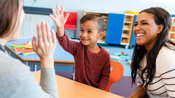 Parent and elementary school child at school with child high-fiving his teacher