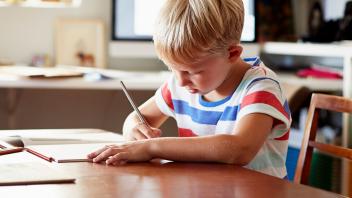 first grade boy writing at kitchen table